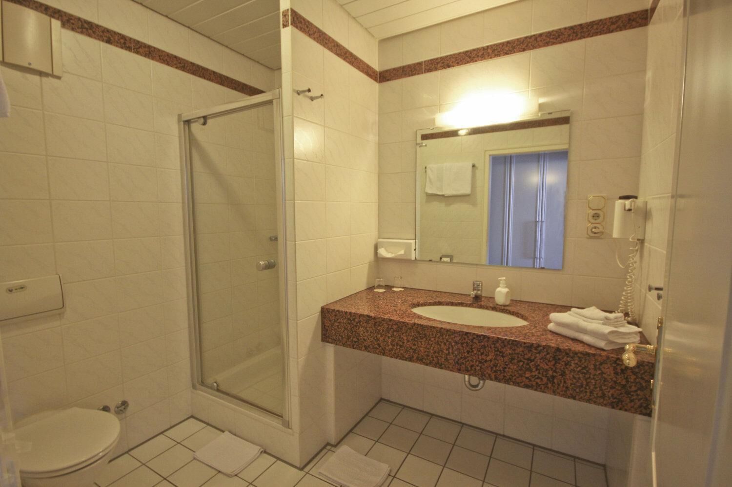 Un baño con cabina de ducha de vidrio, un lavabo con encimera de granito, un espejo y un teléfono.