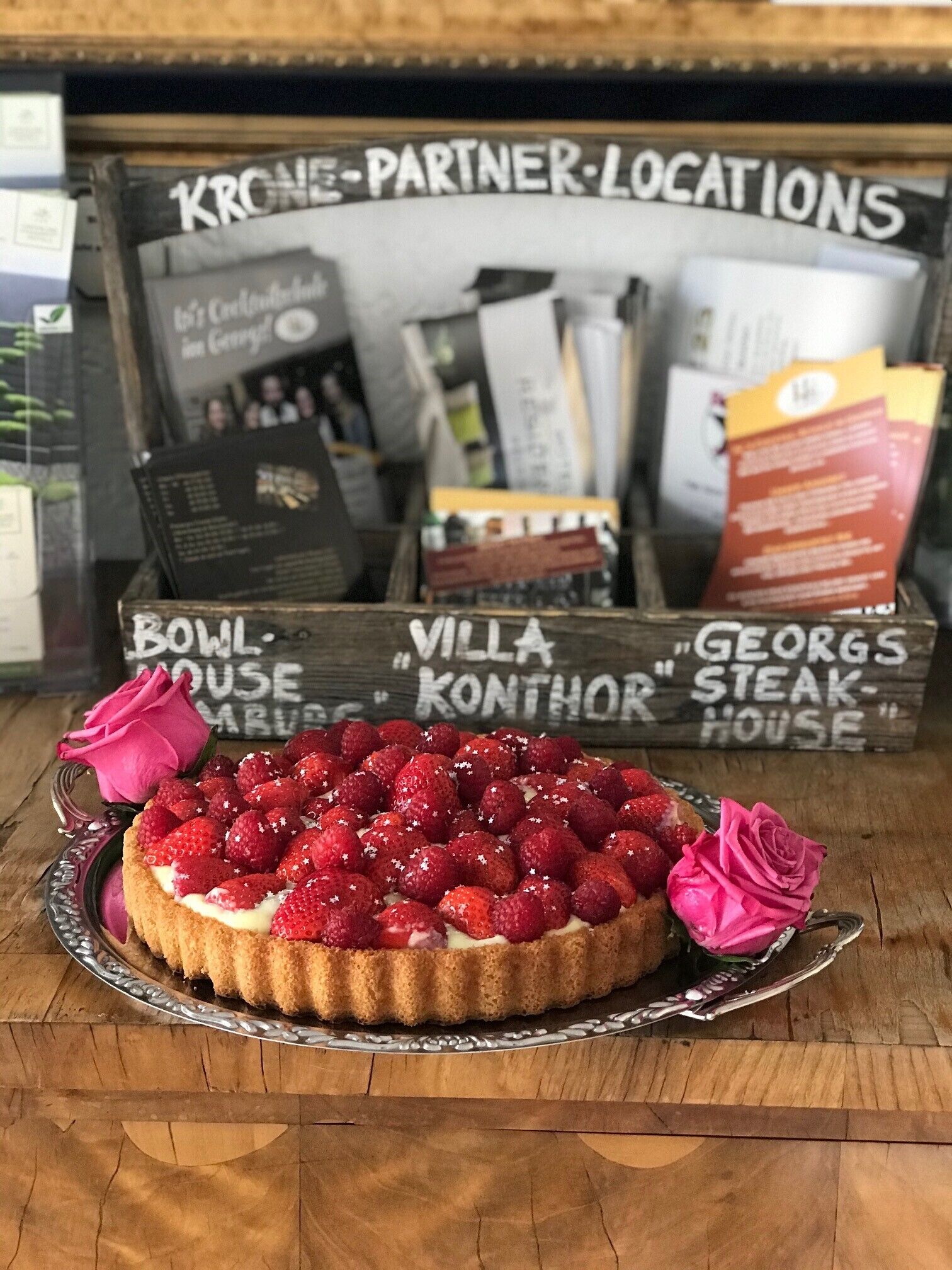 Un dessert aux fraises et aux roses, présenté sur une assiette, avec une table en bois et un panneau indicateur en arrière-plan.