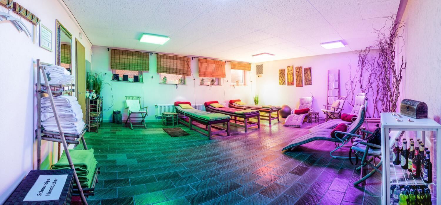 Una habitación con una camilla de masaje, sillas, una mesita y un estante con botellas.