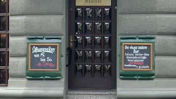 A building with a sign reading "Villa Konthor" and a door labeled "3. Villa Konthor." There are two green signs on either side of the door, one with a price and the other with a description of the bar.