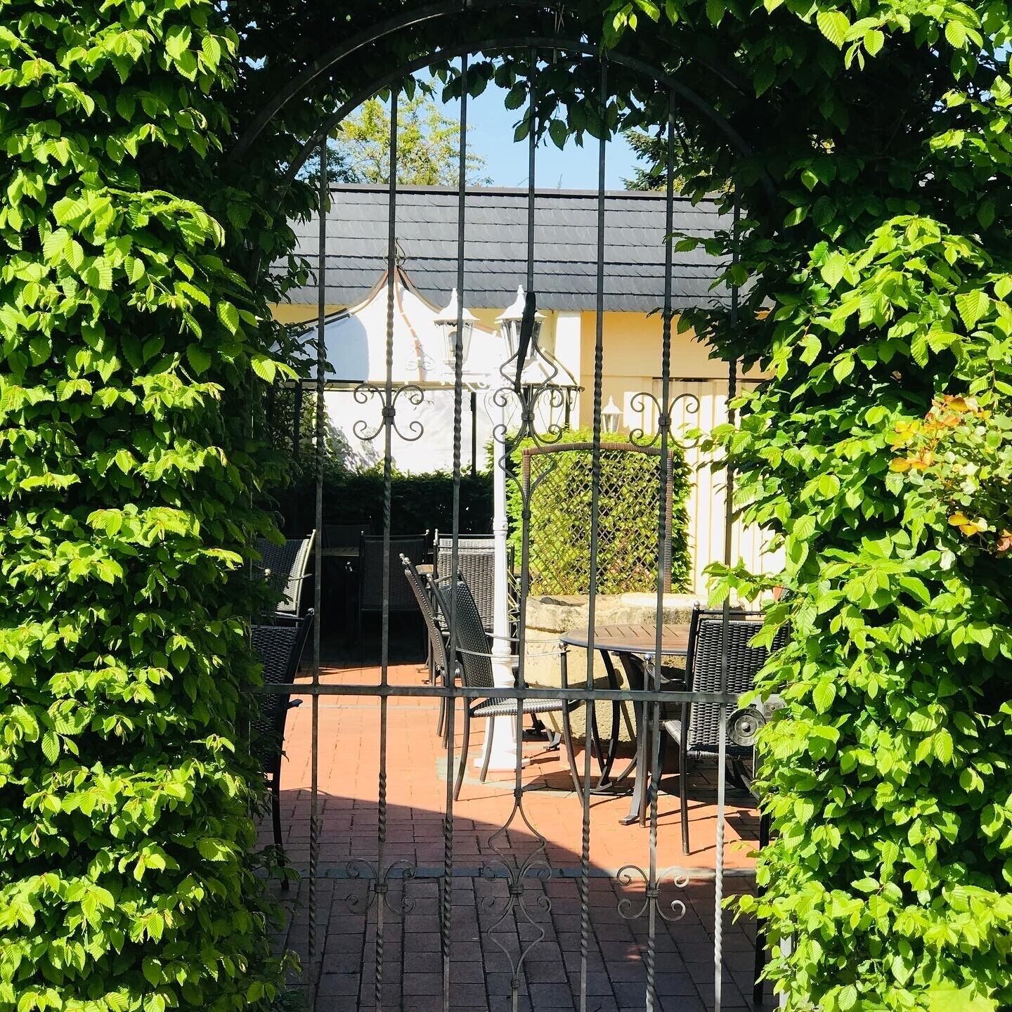 Un'area patio esterna con un cancello in ferro battuto, un tavolo e sedie, e un edificio sullo sfondo.