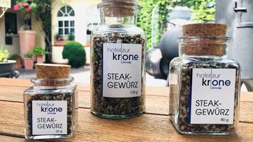 Tres frascos de vidrio con la etiqueta 'Hotel zur Krone' que contienen especias para carne, sobre una mesa de madera al aire libre.