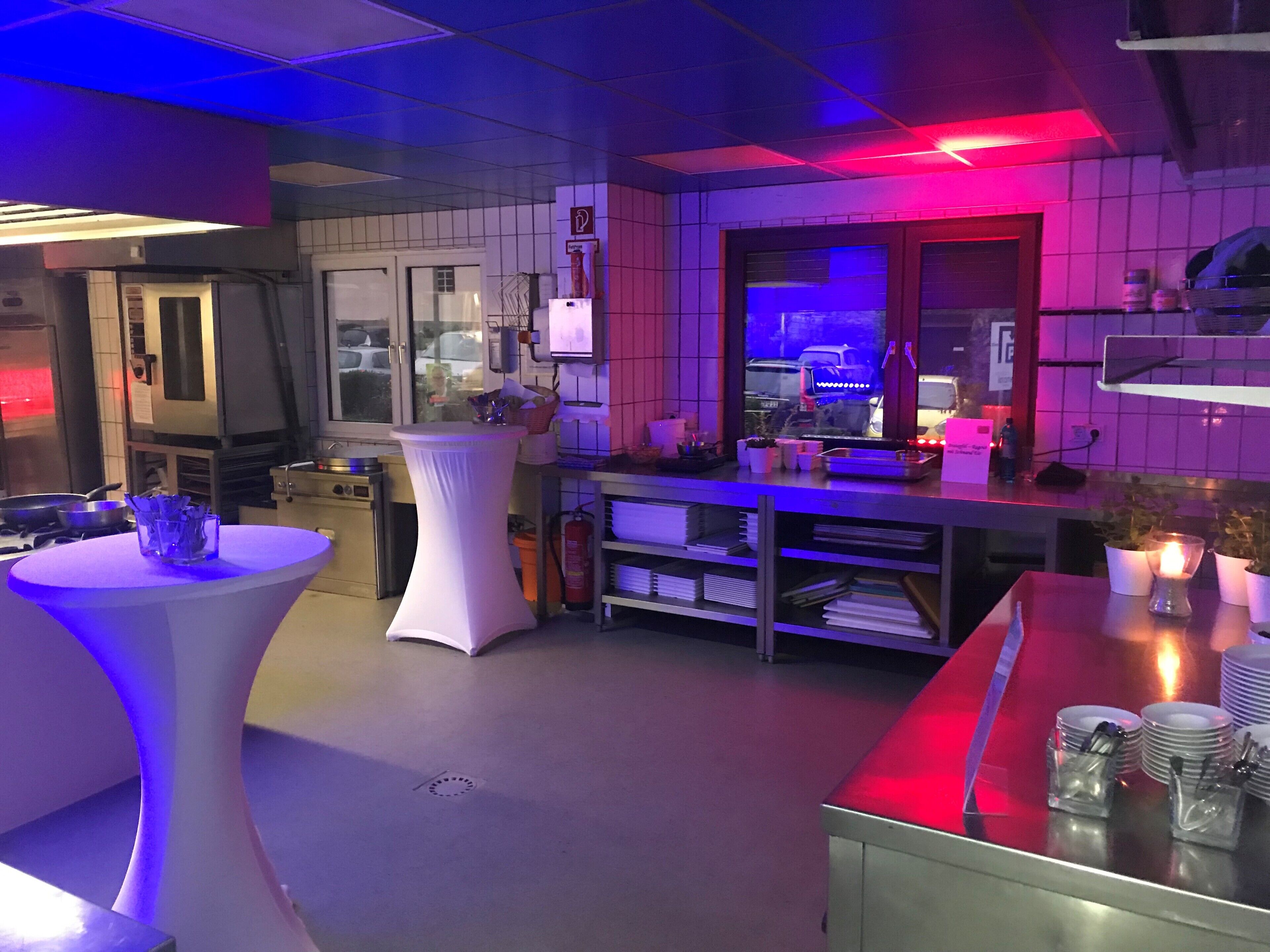 A modern kitchen with a white table, a white pedestal, and a red table. There are various kitchen appliances and utensils visible.