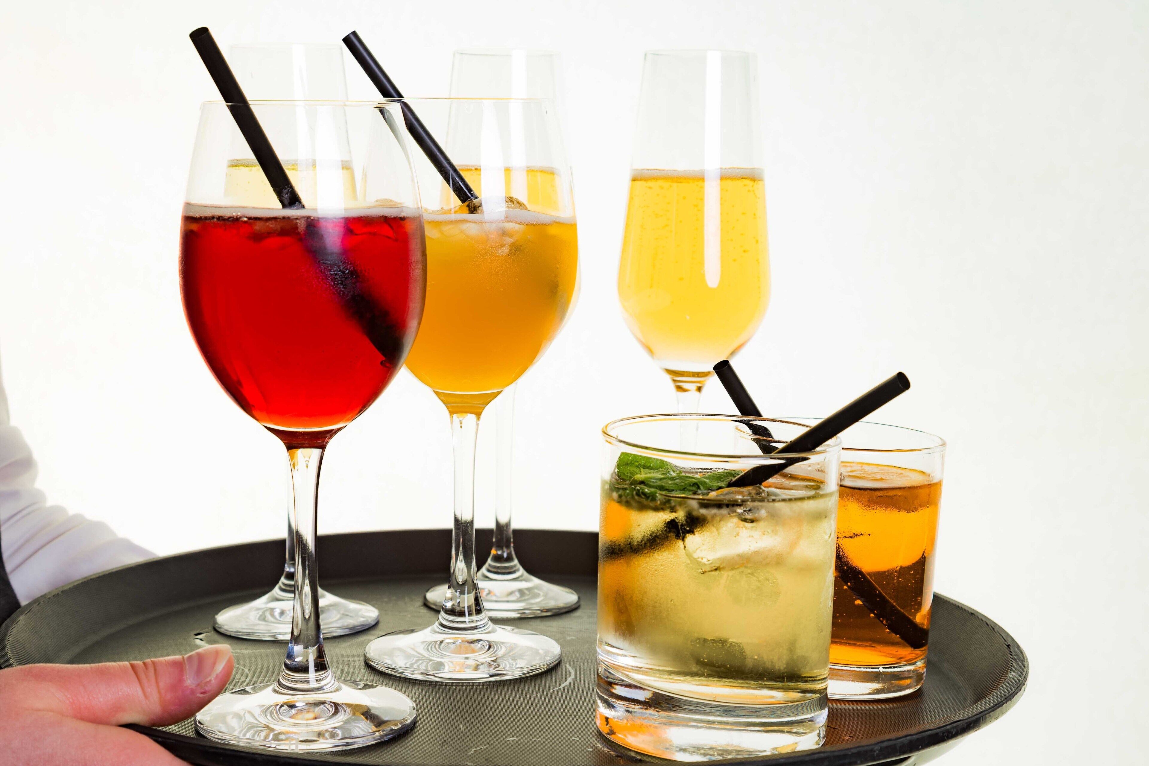 A tray with four glasses of different beverages, including a red drink, a yellow drink, and a clear drink with a mint garnish.