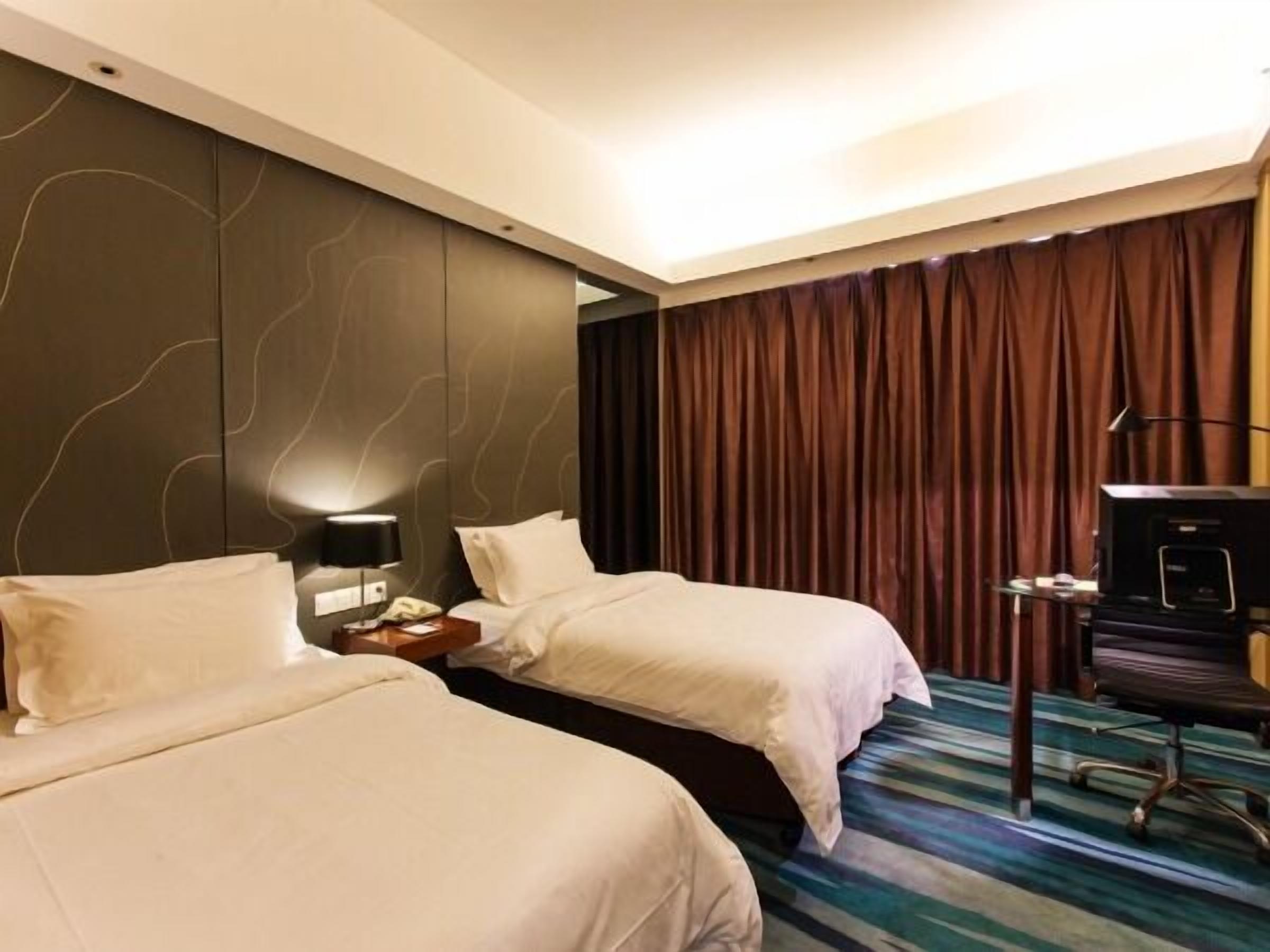 Habitación de hotel con dos camas, un escritorio con televisor y un ventanal con cortinas.