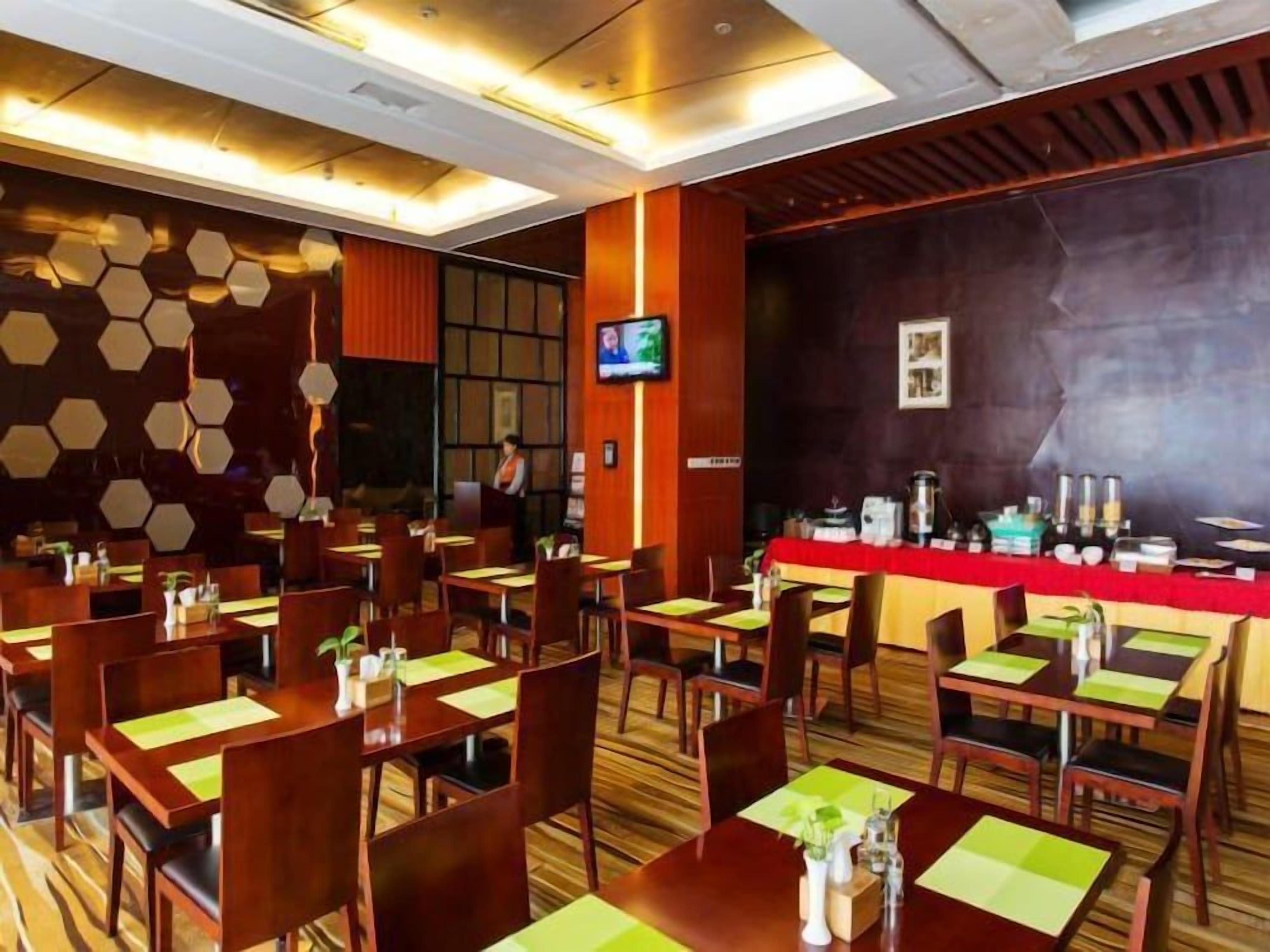 Un comedor de hotel con varias mesas y sillas, una pantalla de televisión y una barra.