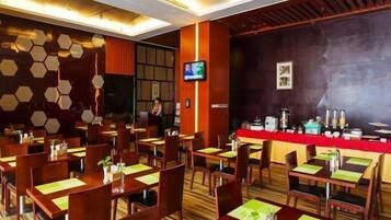 Un comedor de hotel con varias mesas y sillas, una pantalla de televisión y una barra.