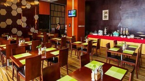 A restaurant with wooden tables and chairs, a counter with a red cloth, and a television mounted on the wall.