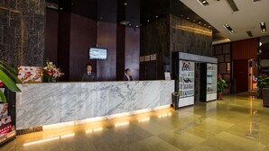 A hotel reception area with marble counters, a digital screen, and a magazine rack.