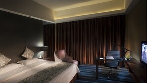 A hotel room with a large bed, a desk with a chair, a television, and a curtain backdrop.