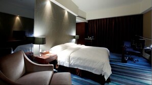 A hotel room with a bed, a desk with a lamp, a chair, a television, and a large window with curtains. - Metropolo Shijiazhuang Yuhua (Shijiazhuang)