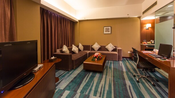 A hotel room with a TV, sofa set, coffee table, desk with computer, and a patterned carpet. - Metropolo Shijiazhuang Yuhua (Shijiazhuang)