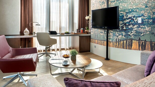 A modern living room with a flat-screen TV, a dining area, and a large window with curtains. - Radisson Blu Hotel Istanbul Asia (Istanbul)