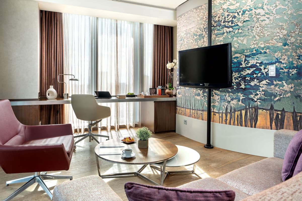 A modern living room with a flat-screen TV, a dining area, and a large window with curtains.