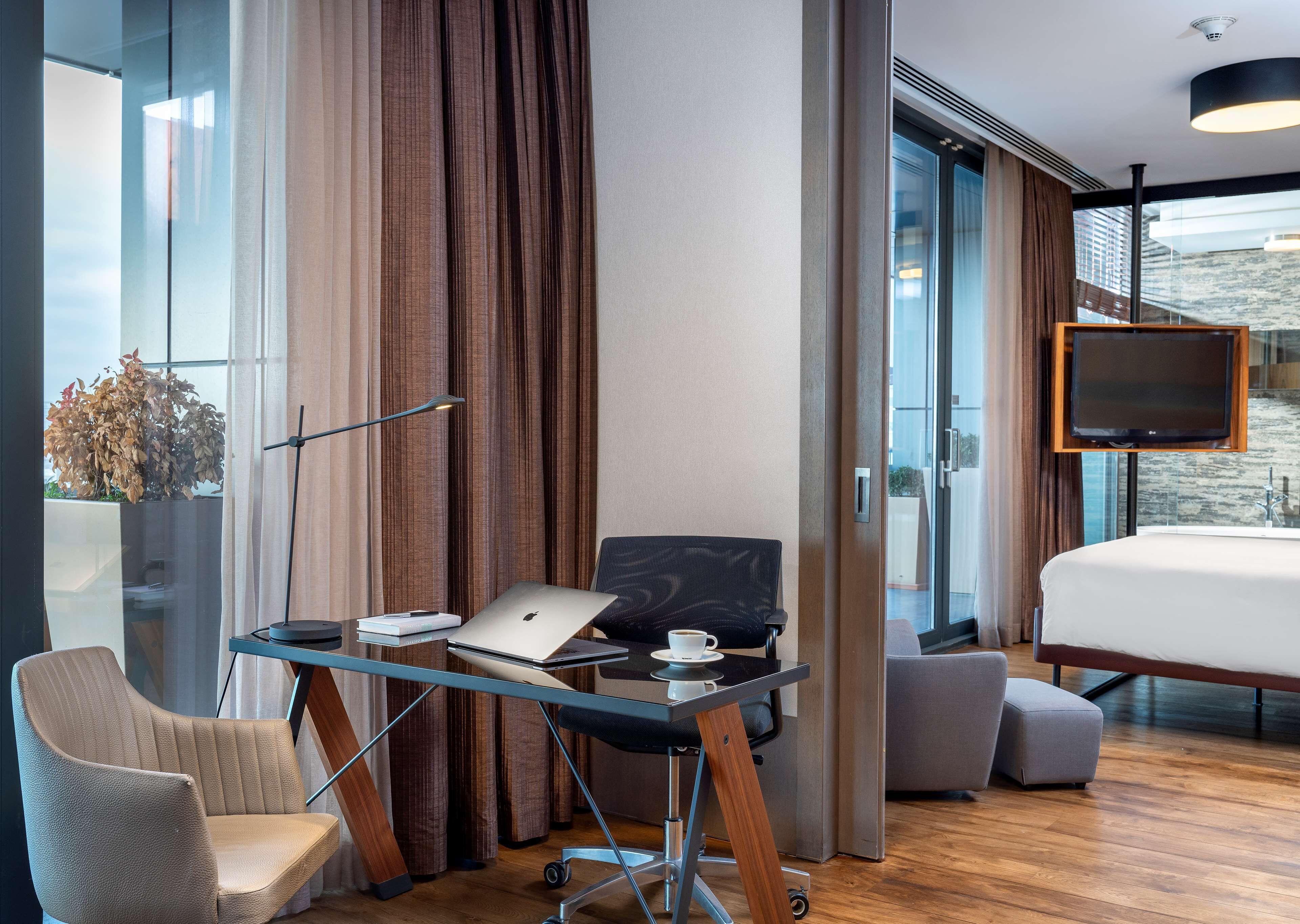 Una habitación de hotel moderna con una cama grande, un escritorio con una computadora portátil, una silla y un televisor.