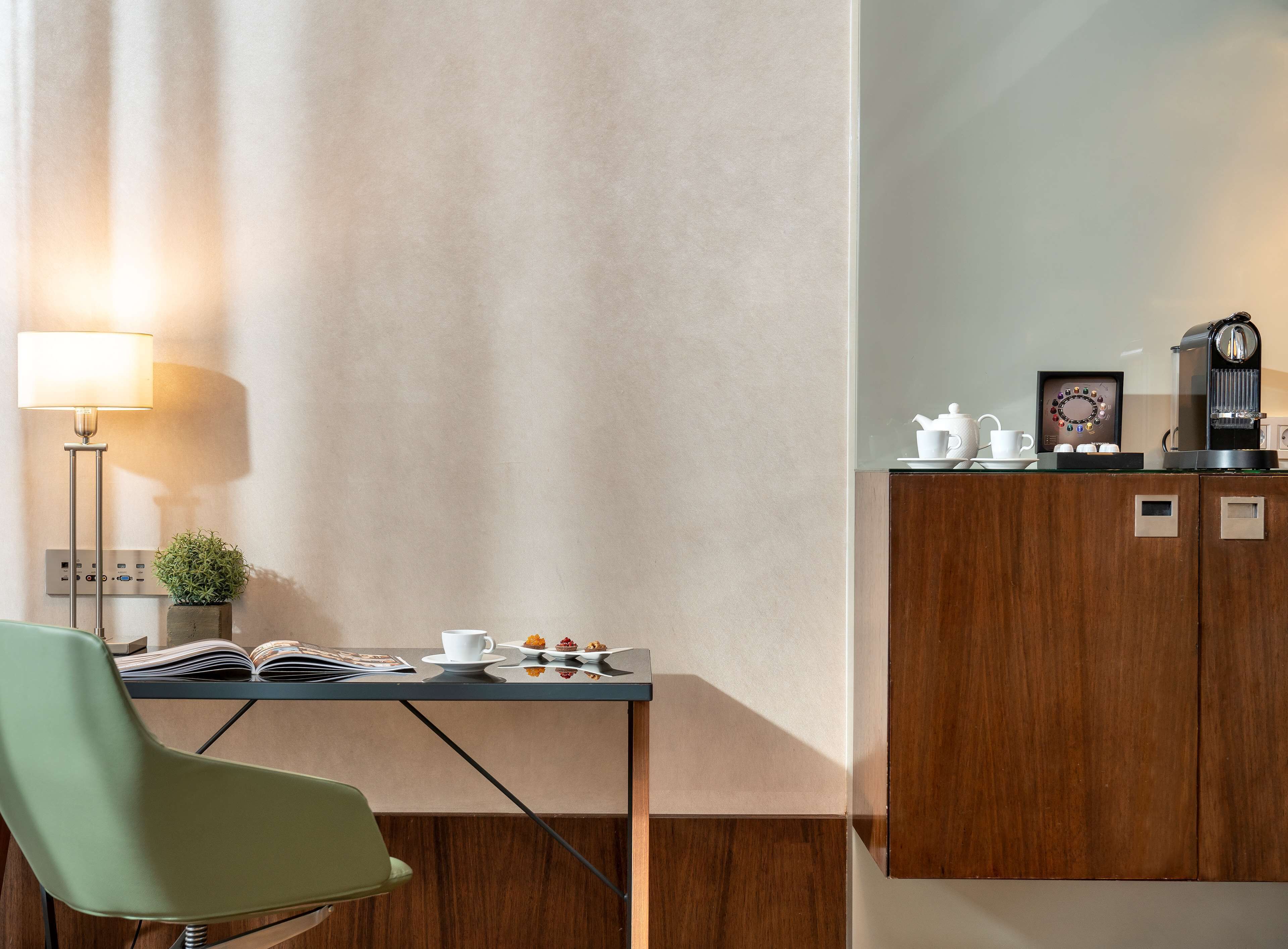 A modern room with a wooden cabinet, a table with a lamp, a chair, and a coffee machine.
