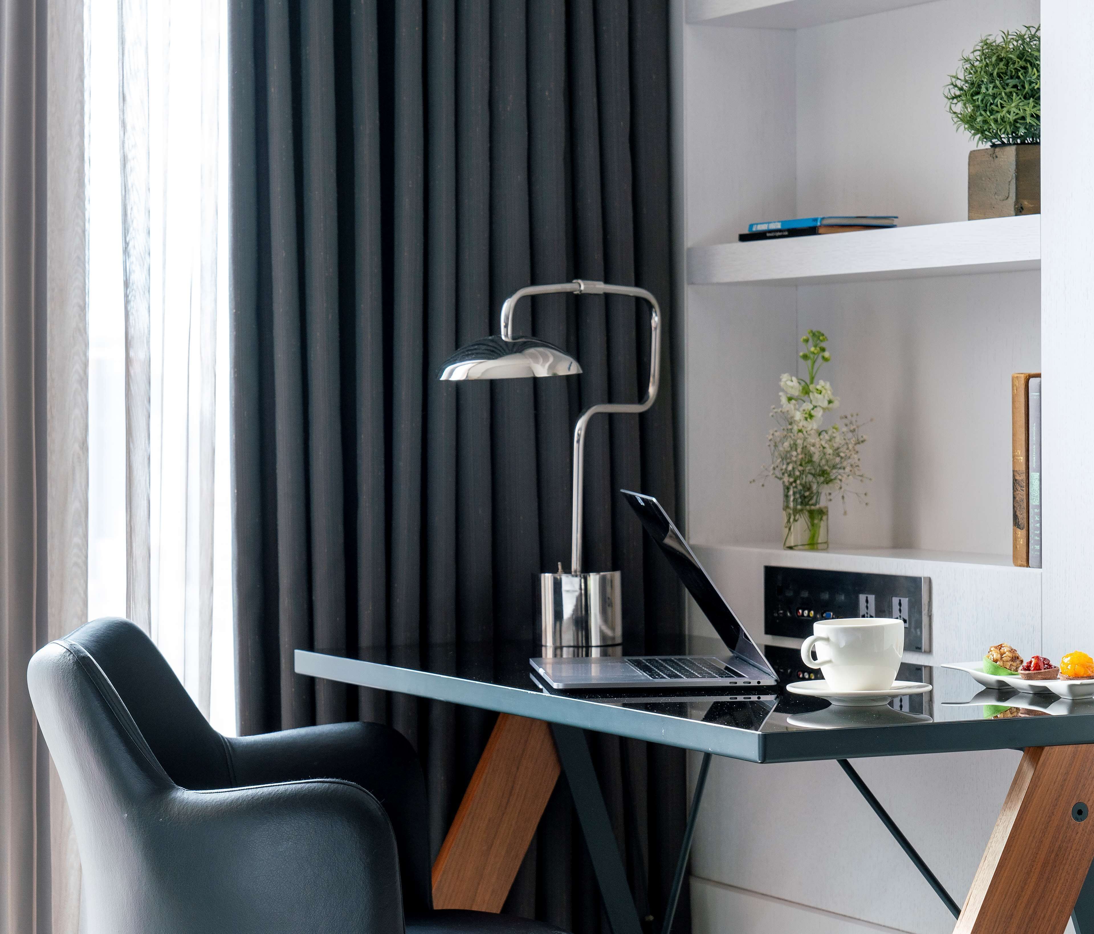 A modern office space with a black leather chair, a glass desk with a laptop, a white coffee cup, and a decorative plant.