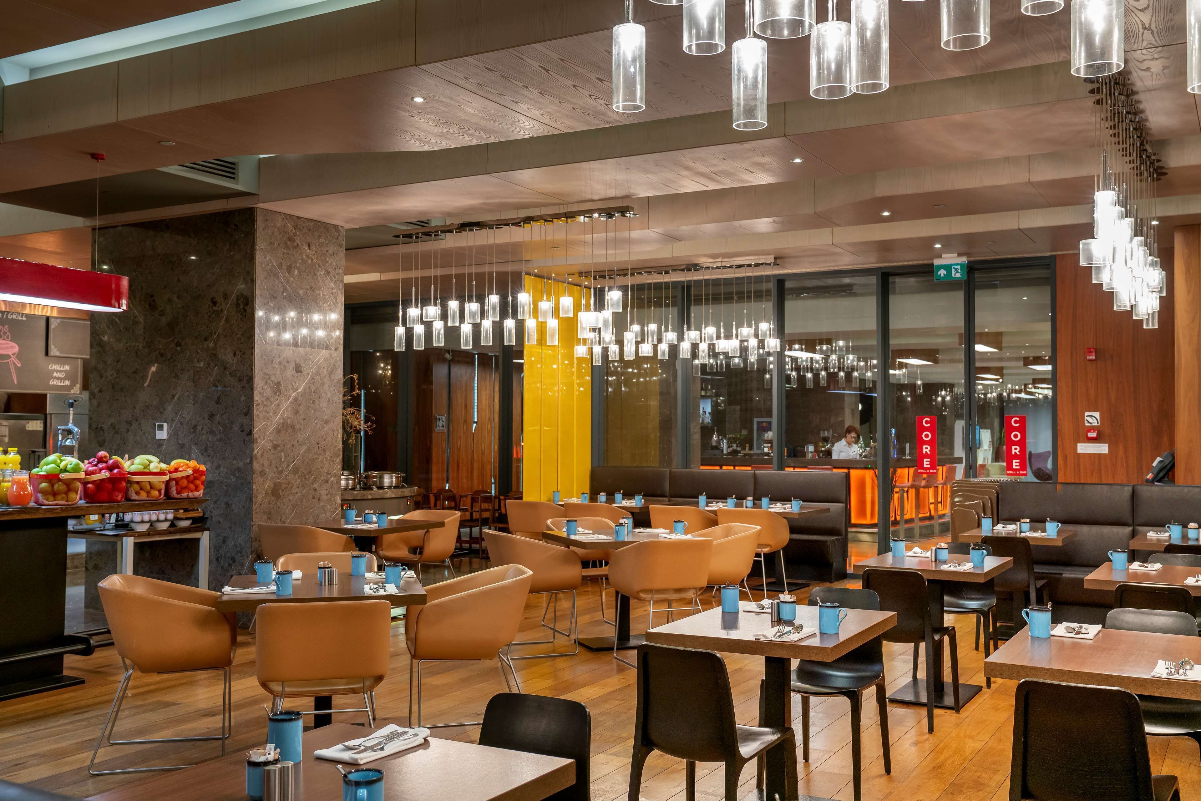 A modern restaurant with wooden floors, multiple seating areas, and hanging pendant lights.