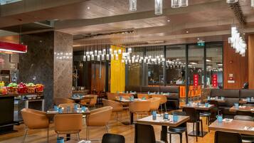 A modern restaurant with wooden floors, multiple seating areas, and hanging pendant lights.