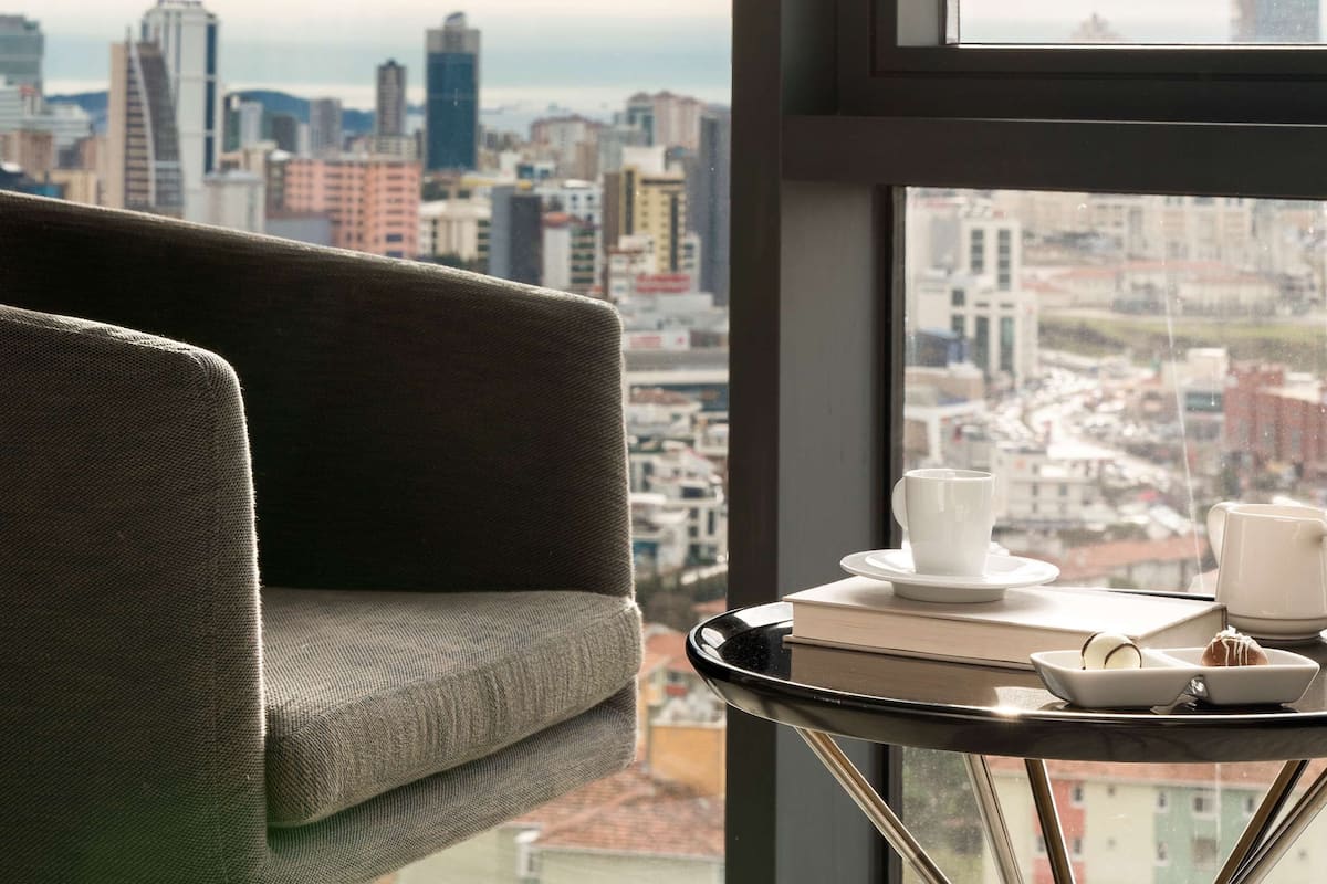 A modern room with a city view, a sofa, a small table with a cup and saucer, and a book.