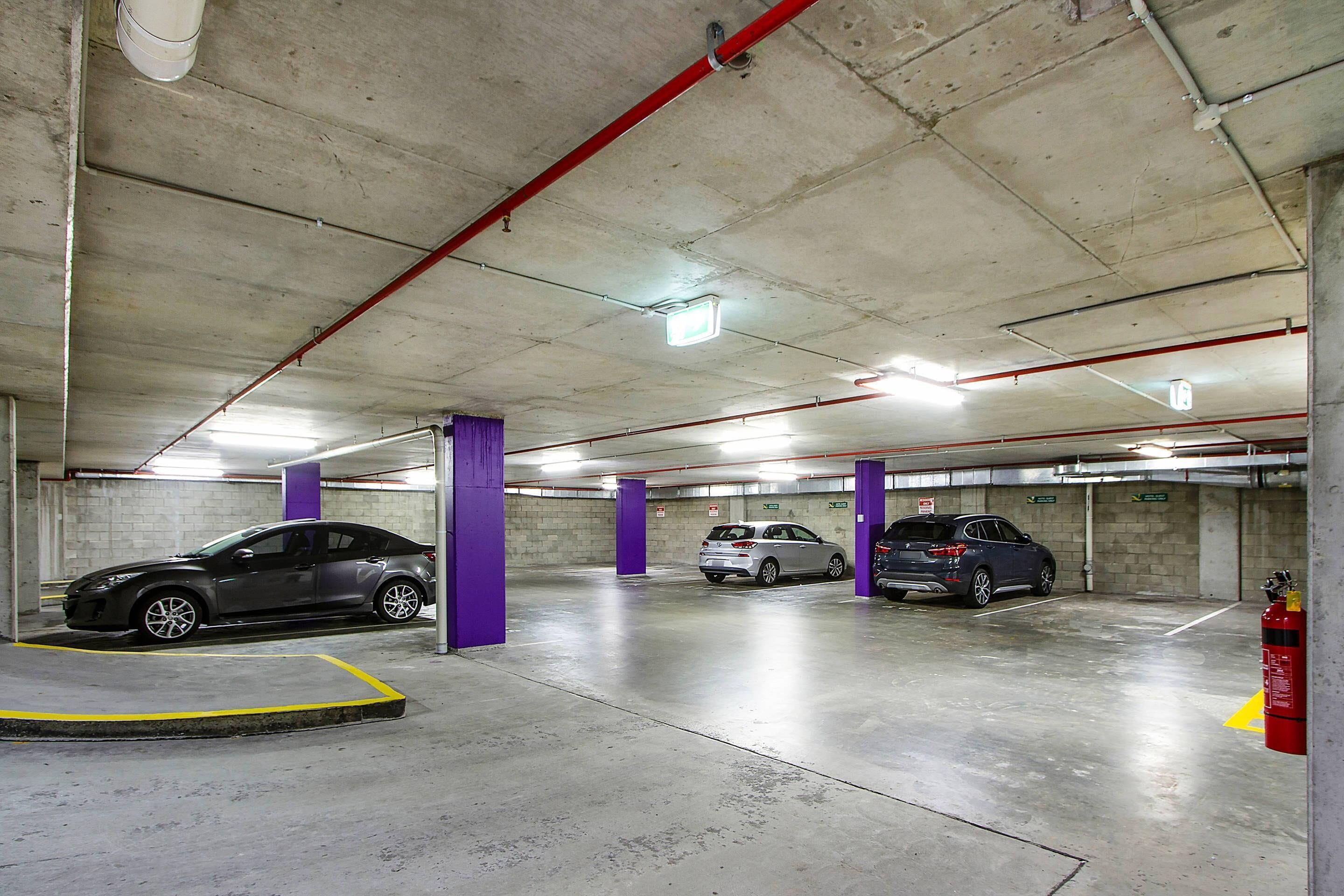 A multi-level parking garage with cars parked in designated spaces, concrete pillars, and overhead lighting.