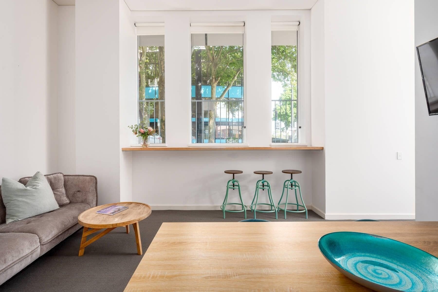 A modern living room with a sofa, a round coffee table, a wooden dining table, and a set of bar stools.