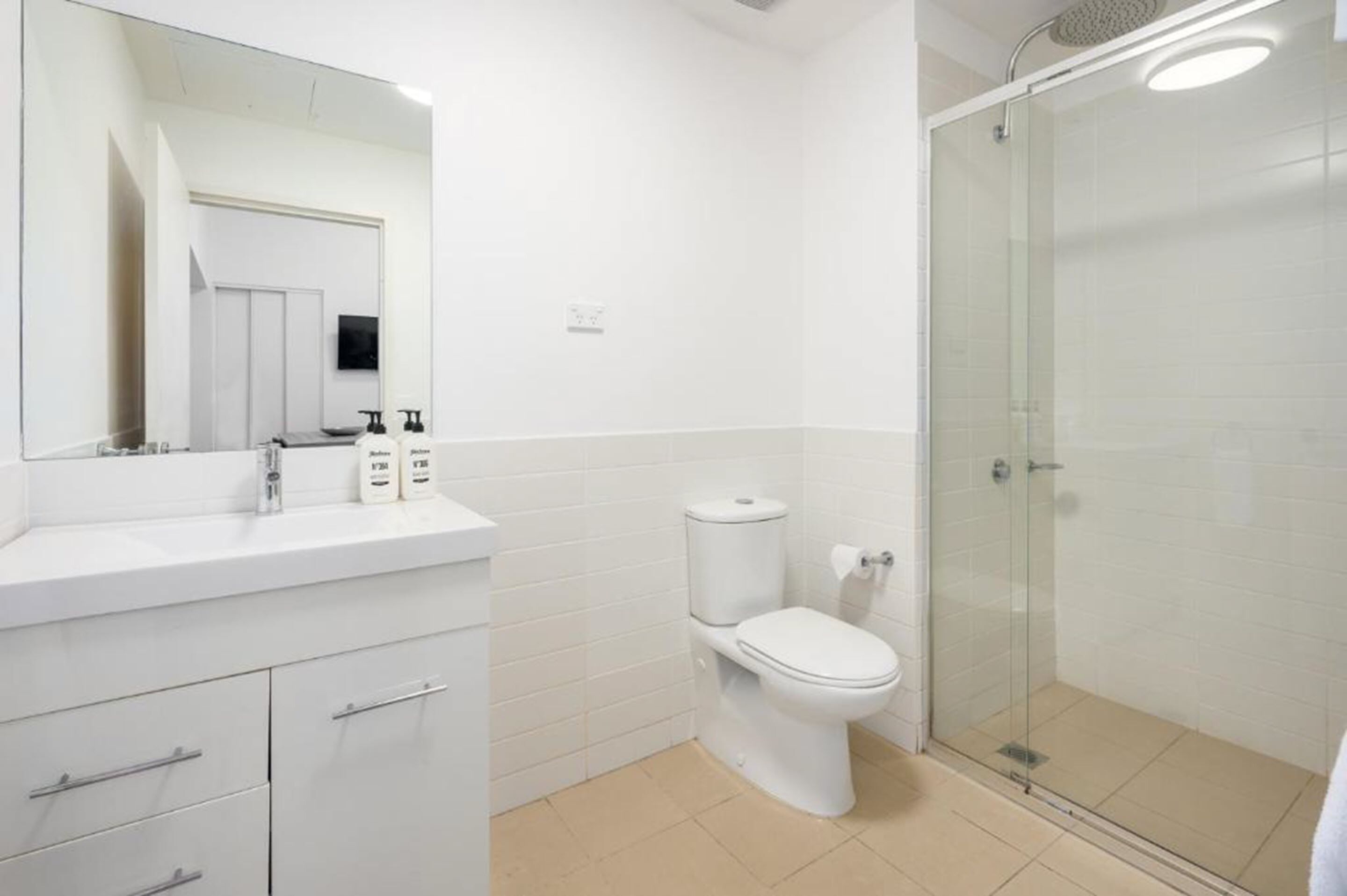 A modern bathroom with a toilet, a glass shower enclosure, a white sink with a mirror, and a tiled floor.
