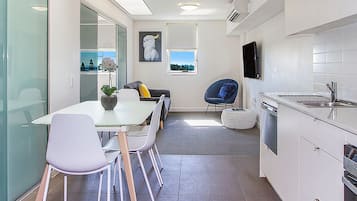 A modern kitchen with white cabinets, a dining area with a table and chairs, a blue chair, and a view of the outdoors through a window.