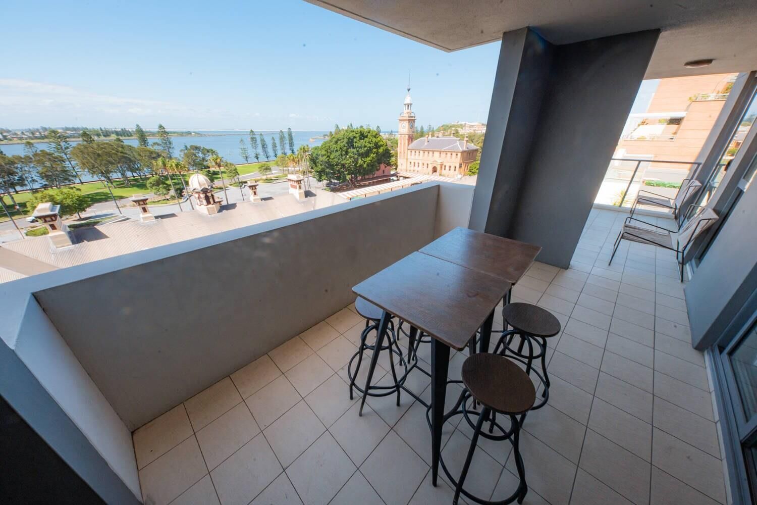 A balcony with a table and chairs, a view of a body of water, and a clock tower in the background.