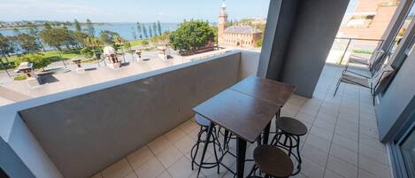 A balcony with a table and chairs, a view of a body of water, and a clock tower in the background.