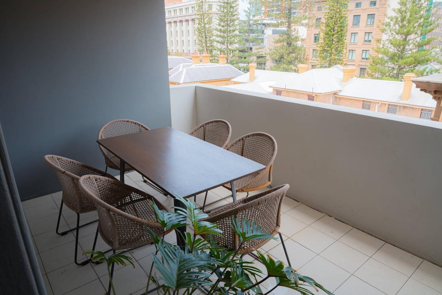 A balcony with a table and chairs, potted plants, and a view of buildings.