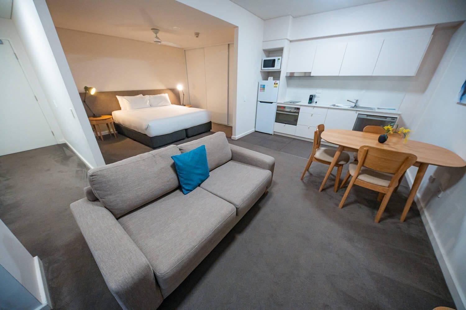 A compact room with a bed, a sofa, a dining table with chairs, and a kitchenette.