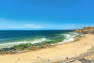 Una playa con aguas azules cristalinas, orilla arenosa y un promontorio rocoso.