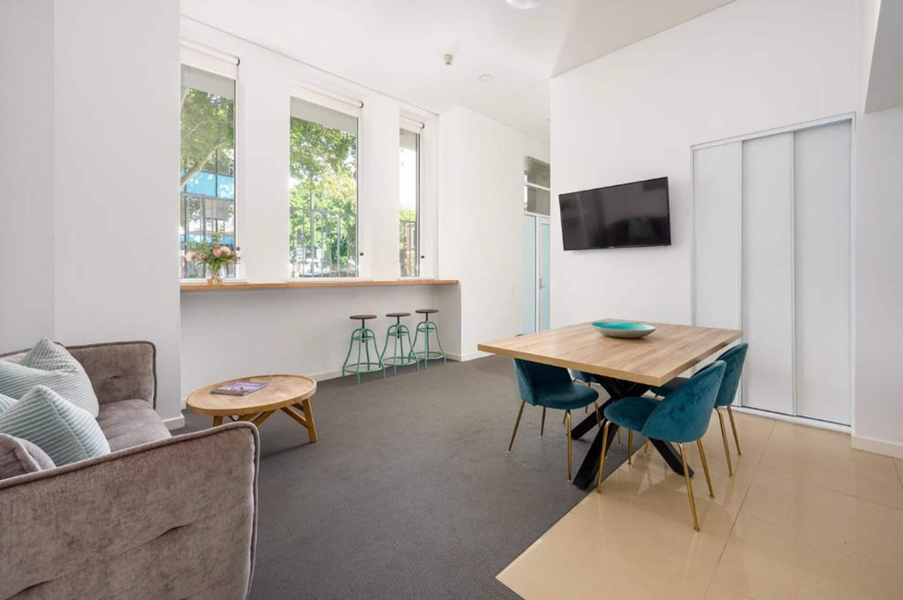 A modern living room with a sofa, a coffee table, a dining table with chairs, and a TV mounted on the wall.
