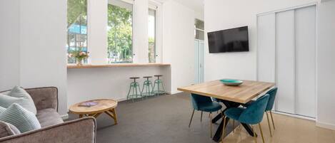 A modern living room with a sofa, a coffee table, a dining table with chairs, and a TV mounted on the wall.