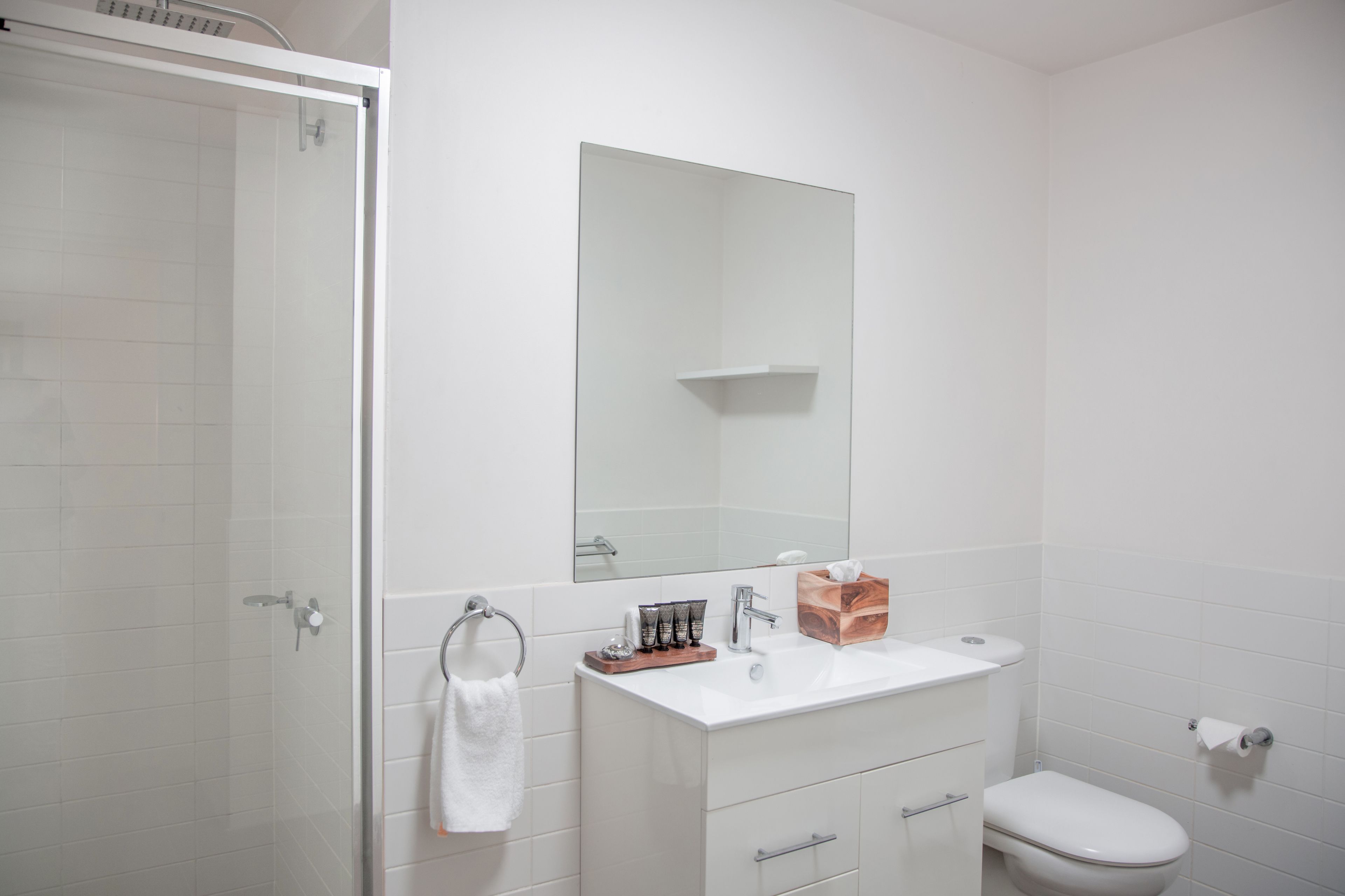 A modern bathroom with a glass shower enclosure, a white sink with a mirror above it, and a toilet.