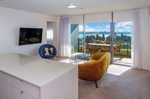 Una habitación moderna con un amplio ventanal corredero que da a un balcón con vista a una masa de agua y un paisaje lejano.