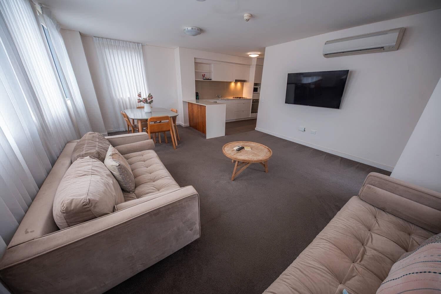 A modern living room with a sofa, a round coffee table, and a TV mounted on the wall.