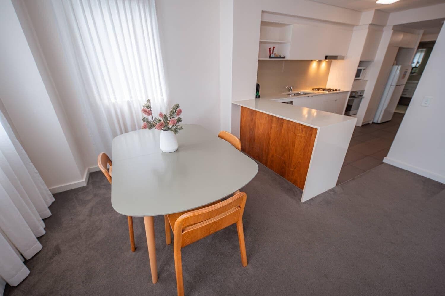 A modern kitchen with white cabinets, a central island, and a dining area with a table and chairs.