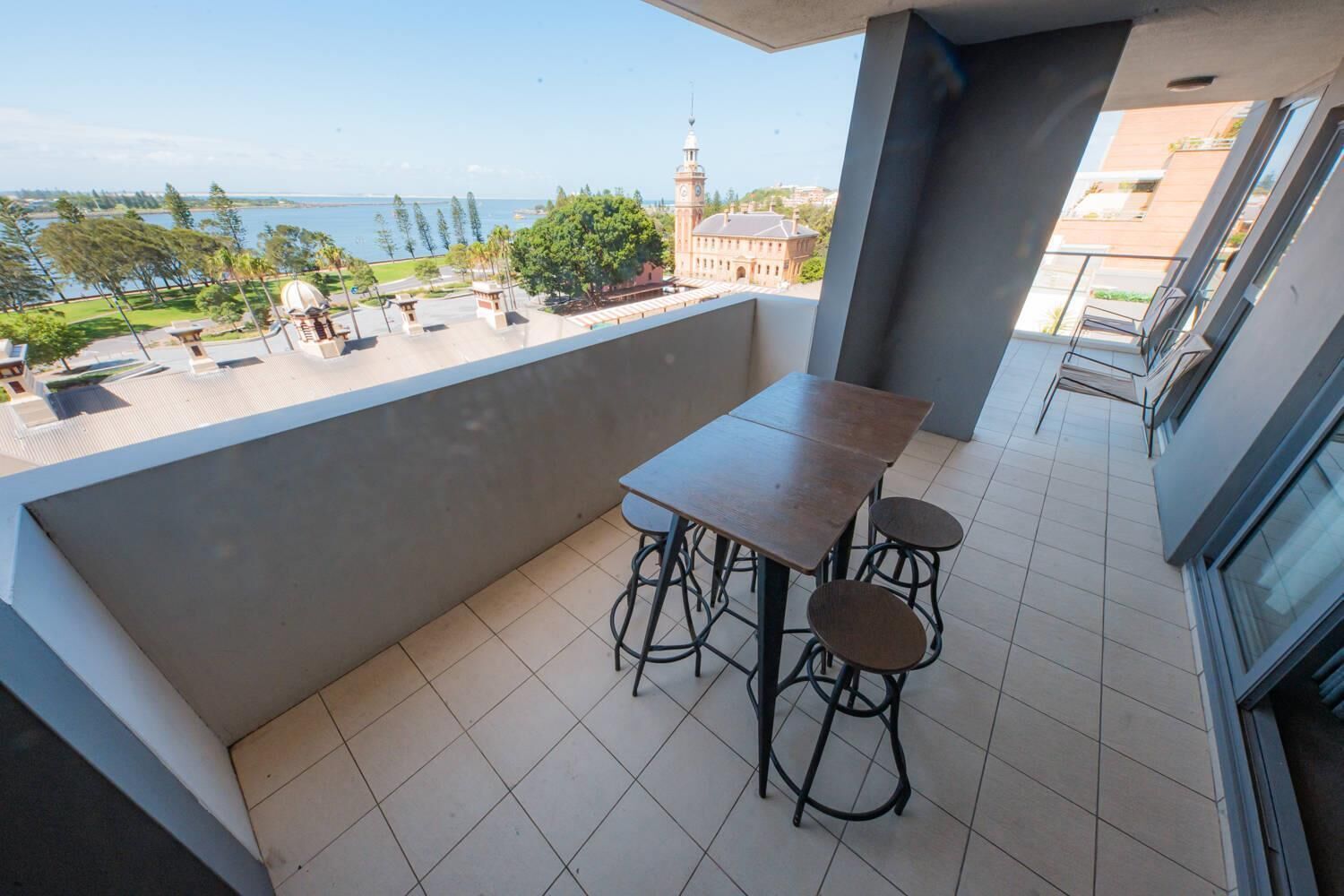A balcony with a table and chairs, a view of the sea, and a building with a clock tower in the background.