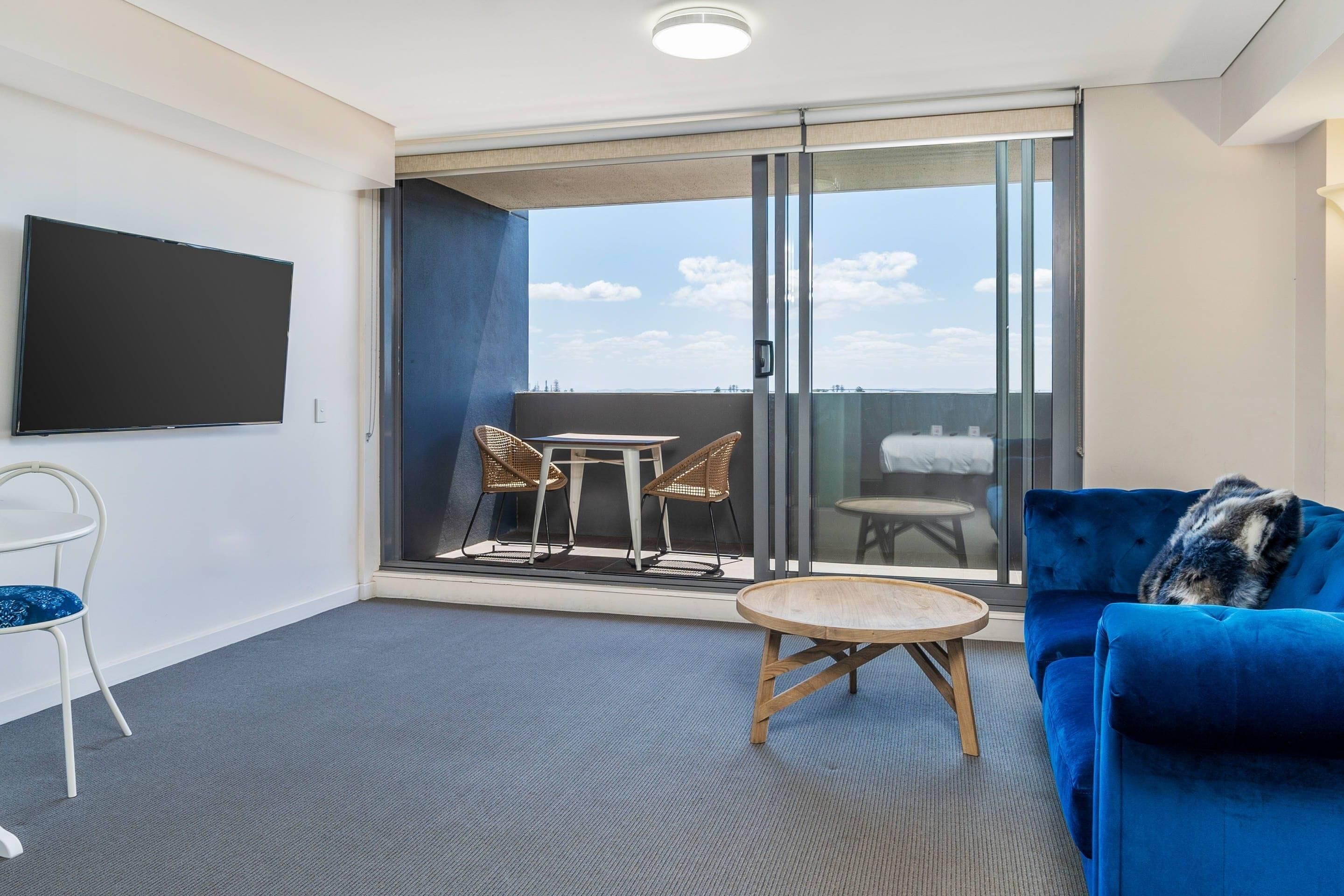 A modern room with a blue sofa, a round wooden table, wicker chairs, and a large TV on the wall.
