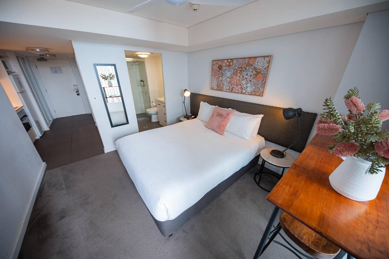 A hotel room with a bed, bedside table, lamp, and a painting on the wall.