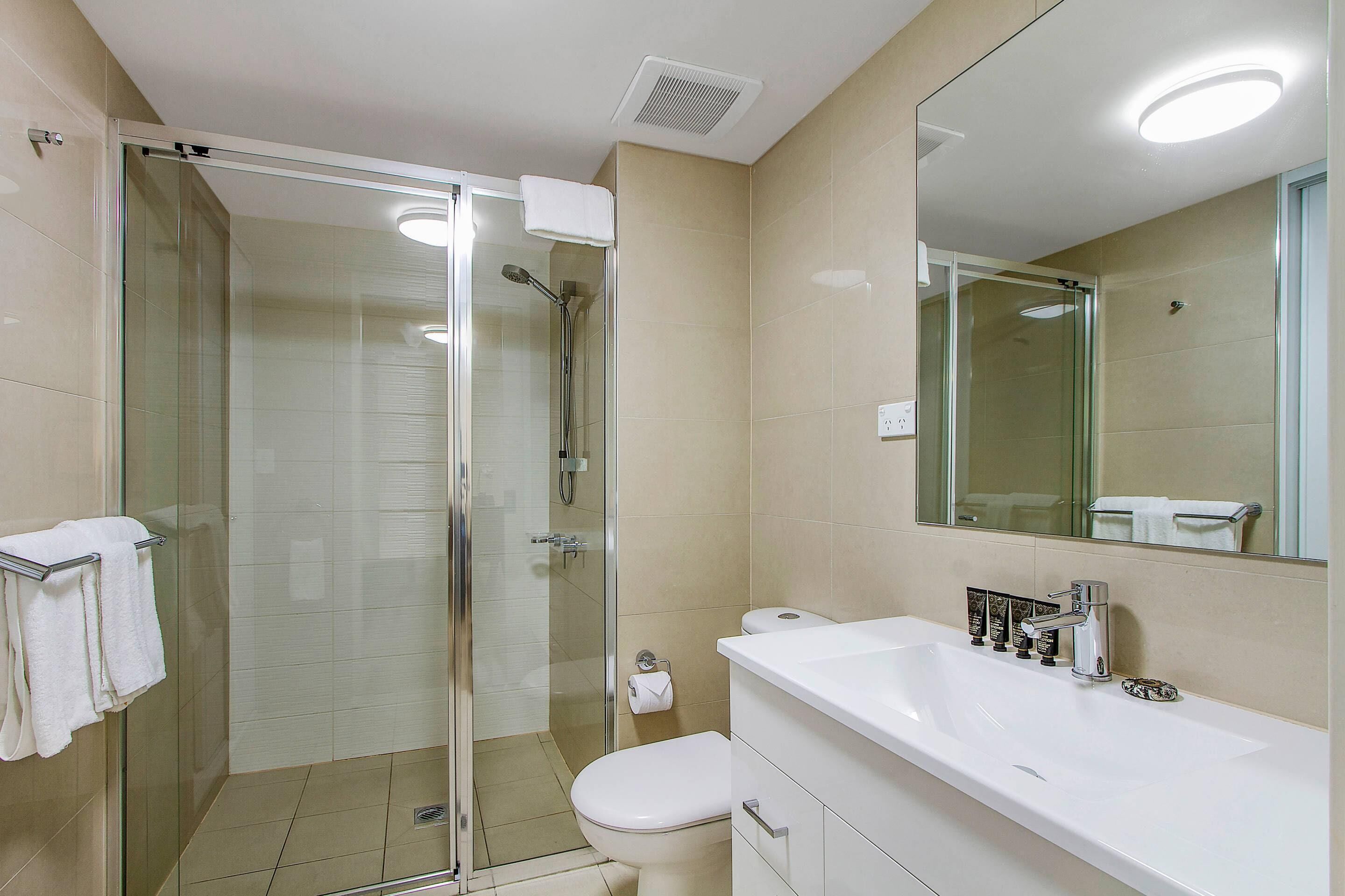 Une salle de bain moderne avec une douche à parois de verre, un lavabo blanc et un grand miroir.