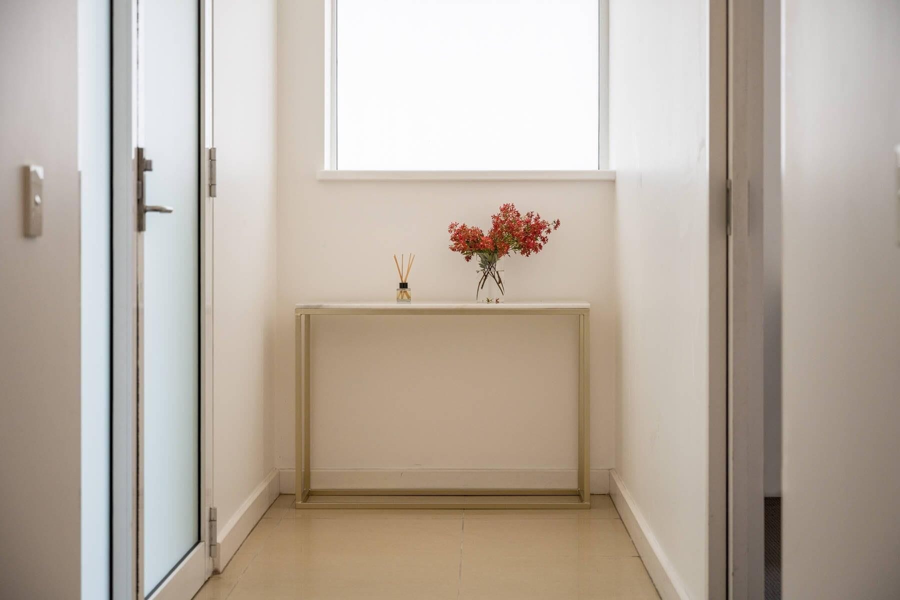 Een gang met een witte console tafel, een raam en een deur.