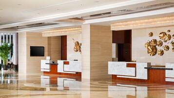 A modern hotel lobby with marble reception desks, a large gold decorative wall, and a view of the sea through large windows.