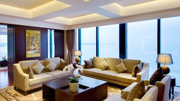A modern living room with two sofas, a coffee table, and a lamp. Large windows offer a view of the water.