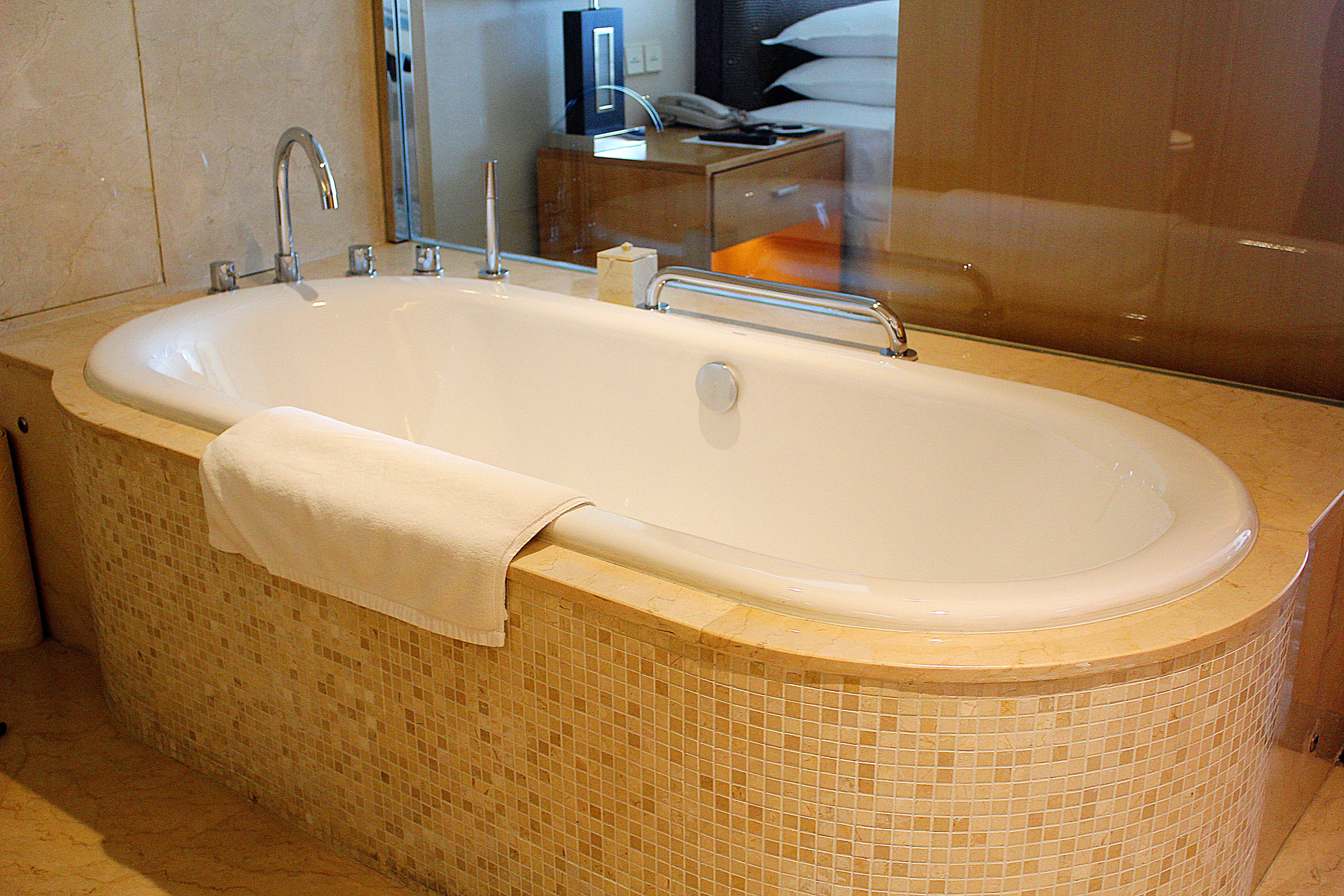 A large, freestanding bathtub with a white towel draped over the side, a chrome faucet, and a tiled surround.