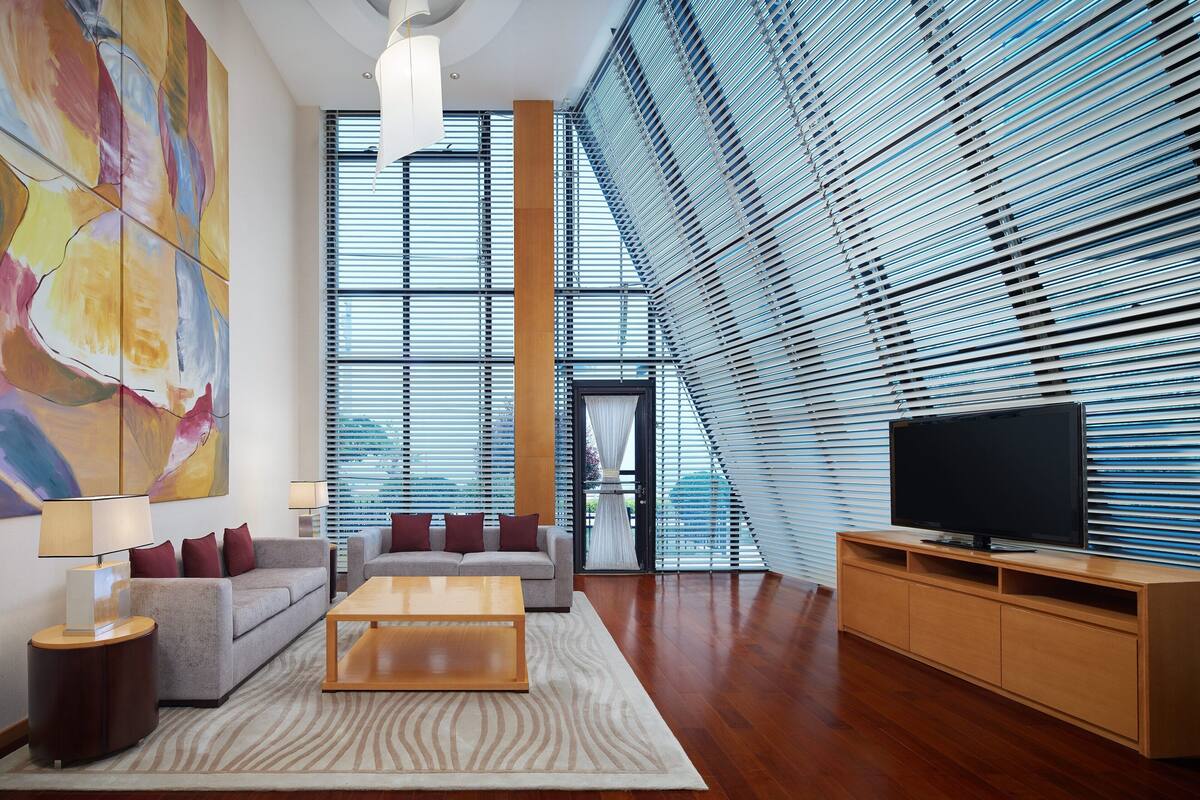 A modern living room with a large abstract painting, a sofa, a coffee table, a TV on a wooden stand, and a patterned rug.