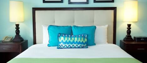 A neatly made bed with a white headboard, two pillows, and a green bedspread. There are two bedside tables with lamps and a phone on one. Three framed pictures are hung on the wall above the bed.
