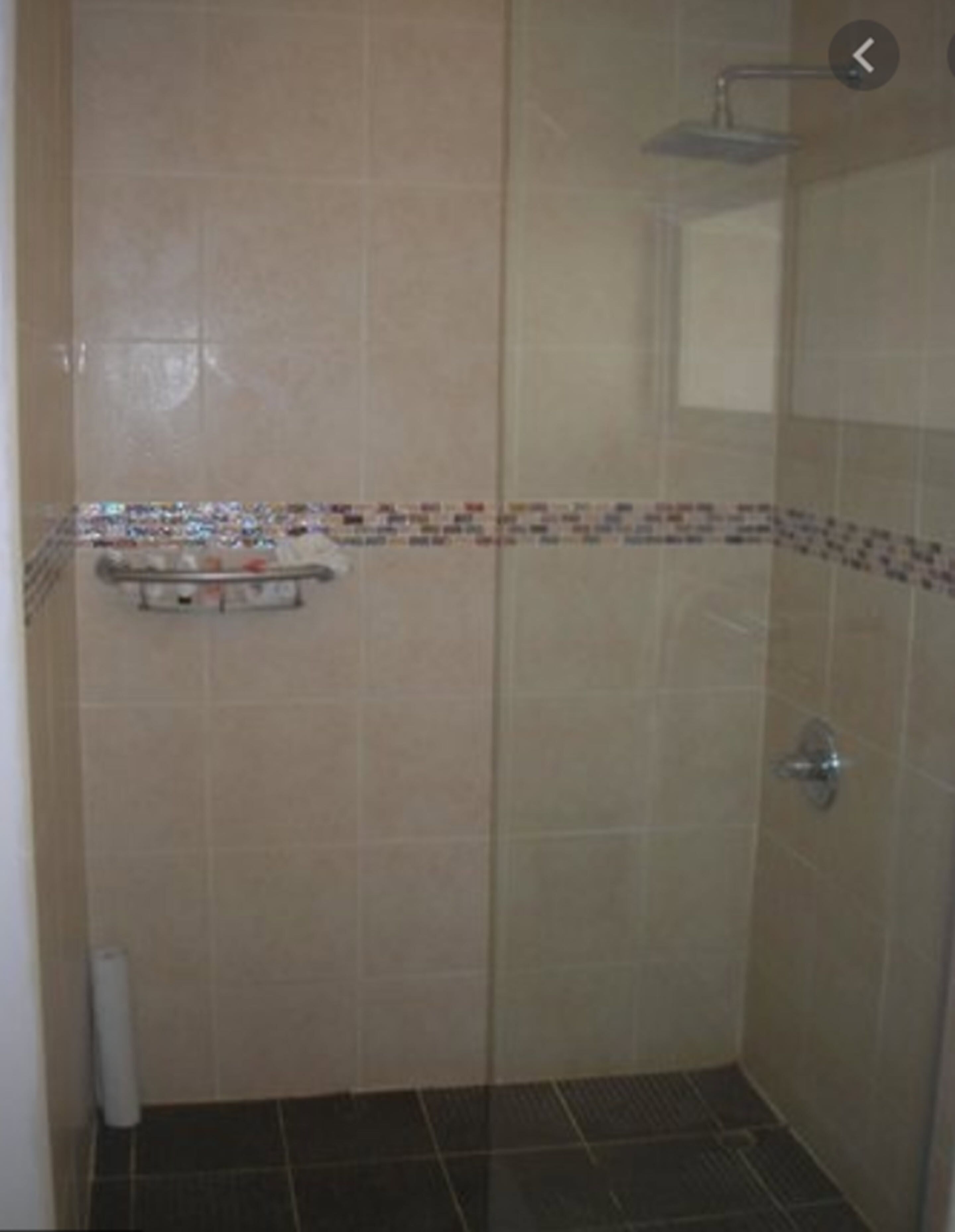 Un espace douche fermé par des parois de verre, doté d’un sol carrelé et d’une étagère pour les articles de toilette.